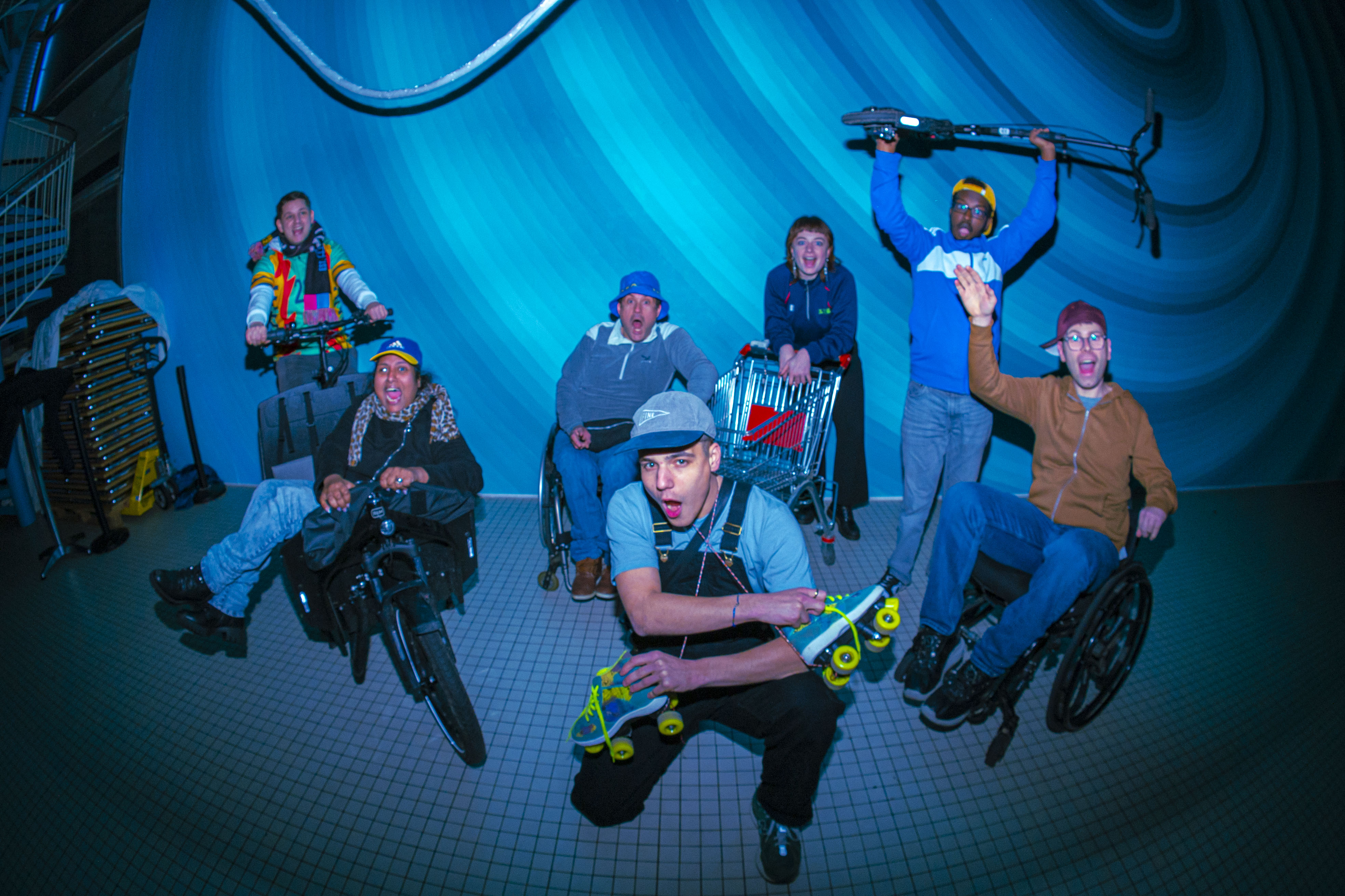 Gruppe von jungen Menschen im Neubad Pool in Rollstühlen und mit Rollschuhen, die drinnen ausgelassen posieren und jubeln. Gruppe von jungen Menschen im Neubad Pool in Rollstühlen und mit Rollschuhen, die drinnen ausgelassen posieren und jubeln.